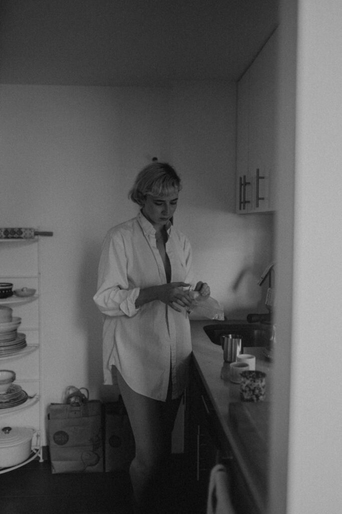 Black and white photo of woman in open white button up shirt in kitchen during intimate couple session New York City