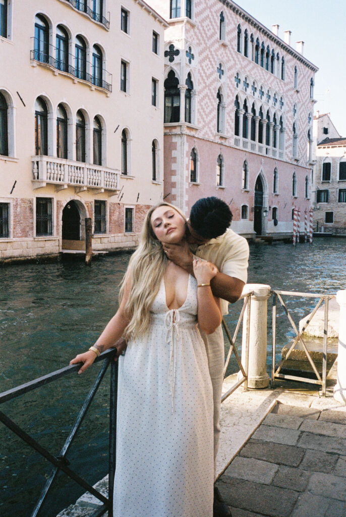 Couple standing beside a Venice canal photographed on film, his hand sensually wrapped around her neck