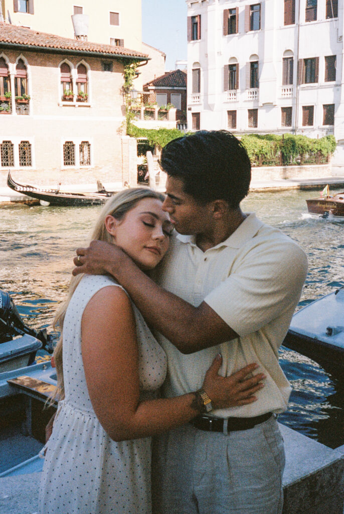 Couple hugging beside a Venice canal photographed on film, his hand gently touching her hair
